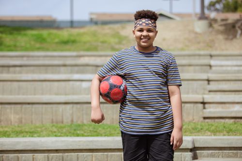 Free Smiling child standing outdoors with a soccer ball, ready to play in the park. Stock Photo
