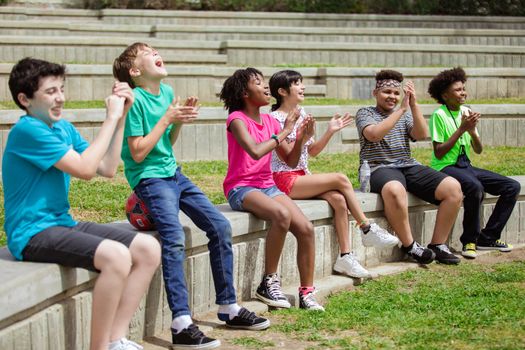 A group of children joyfully clapping and cheering together while sitting outdoors.