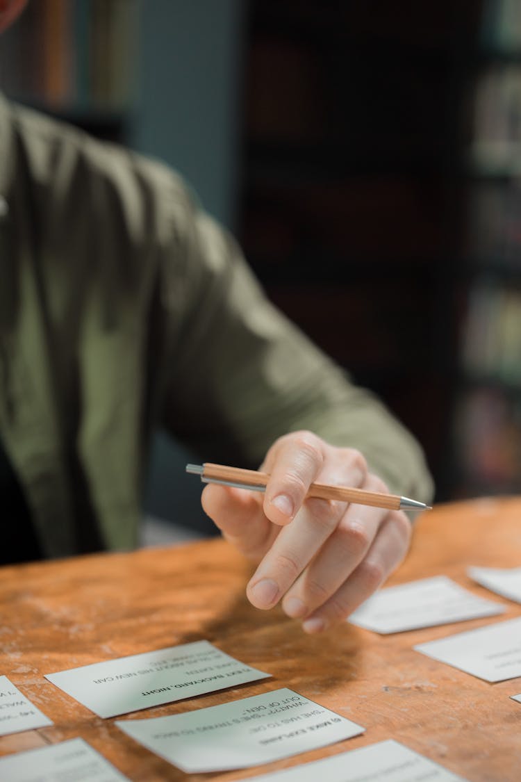 Close-up Of Man Sitting At The Table With Pieces Of Paper And Holding A Pencil