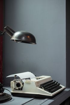 A classic typewriter and desk lamp on a desk in a room with gray walls. Vintage office setup.