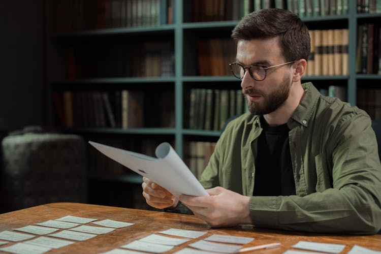 Man In Glasses Sitting At Desk With Paperwork