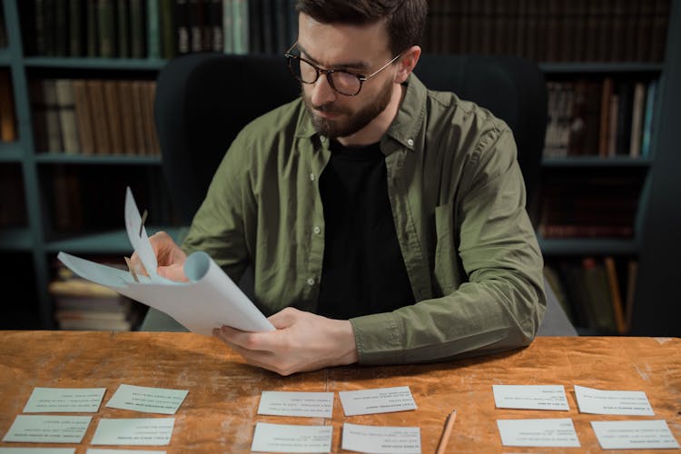 Man In Glasses Sitting At Table With Paperwork And Cards