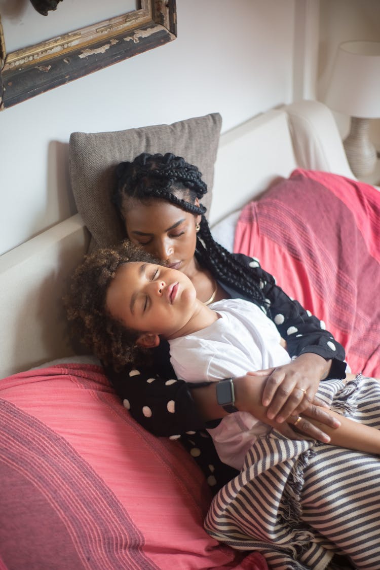 
A Mother Sleeping On A Couch While Hugging Her Child