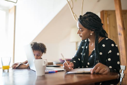 Mother and child working together on a laptop and notepad indoors.