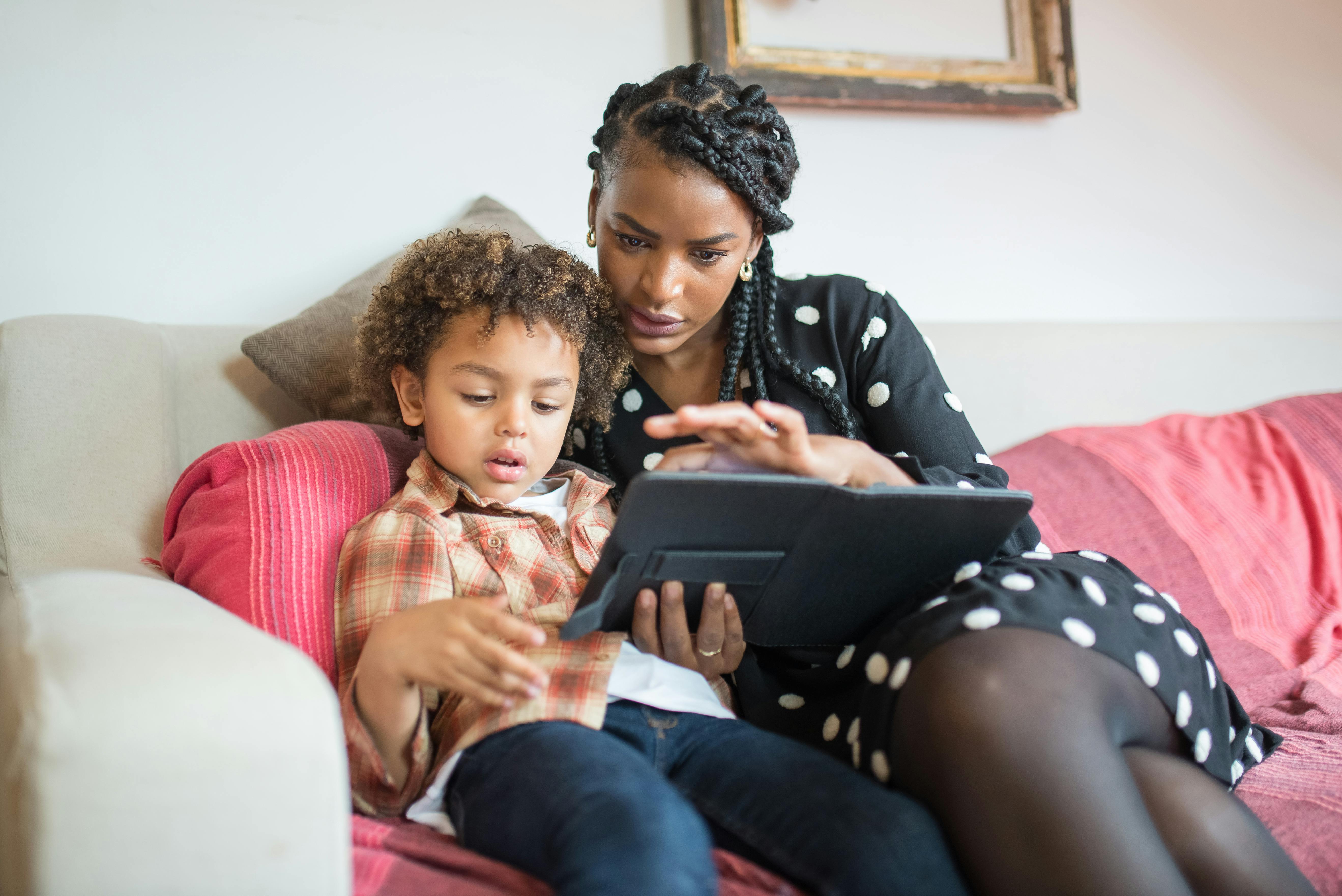 A caring mother and her son using a tablet together on a cozy couch at home.