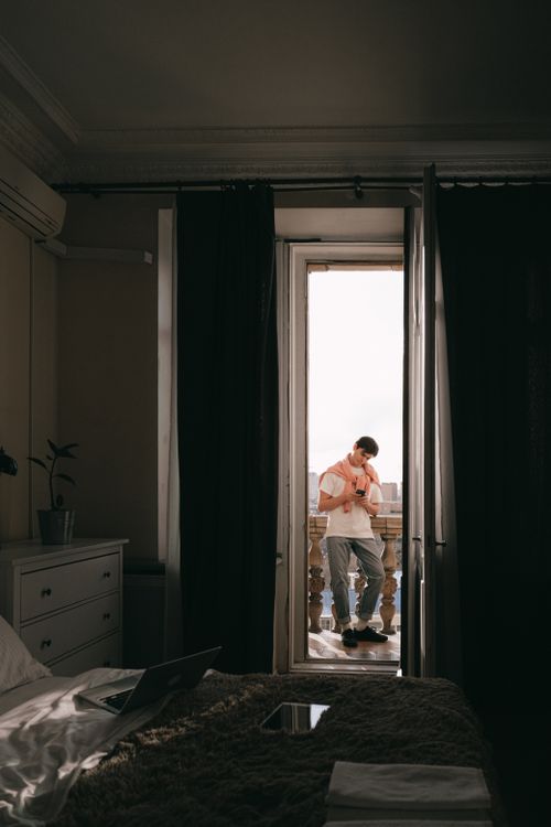 Free A young man casually leaning on a balcony, gazing out from a chic modern room. Stock Photo
