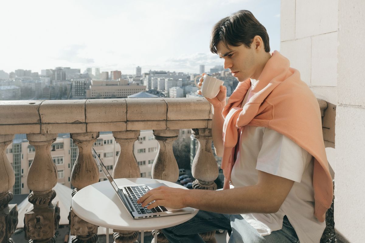 Barbat cu o ceasca de cafea si laptop pe o masuta, cu orasul in fundal