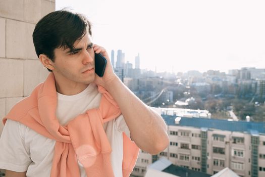 Young adult casually talking on the phone while enjoying a city view from a balcony.