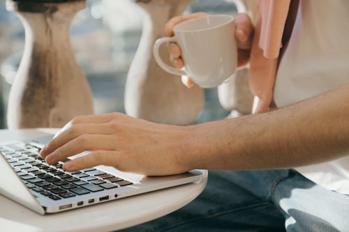 Free Close-up of a person working outdoors with a laptop and coffee in hand. Stock Photo