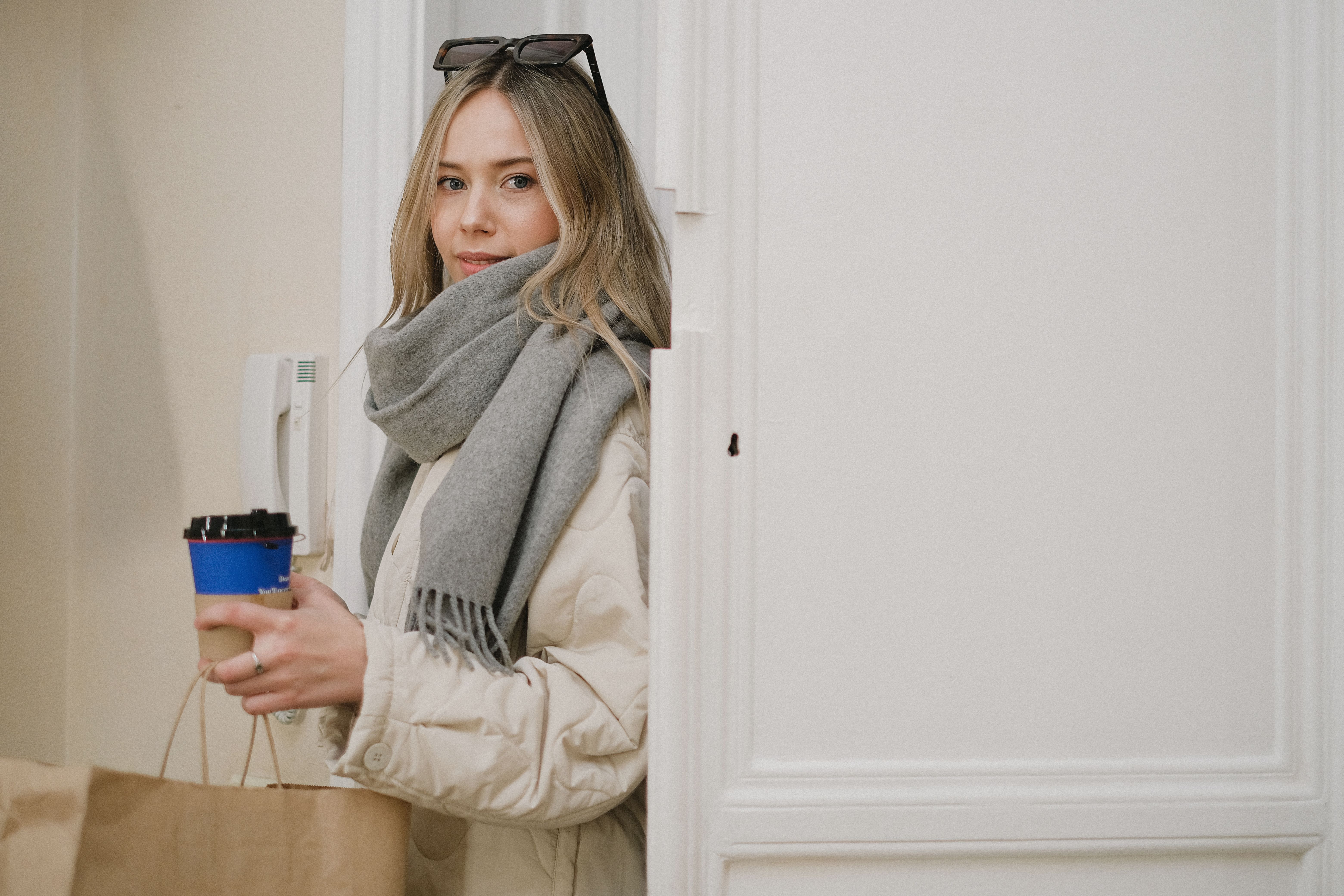 Caucasian woman indoors with coffee cup and shopping bag, dressed warmly in a scarf.