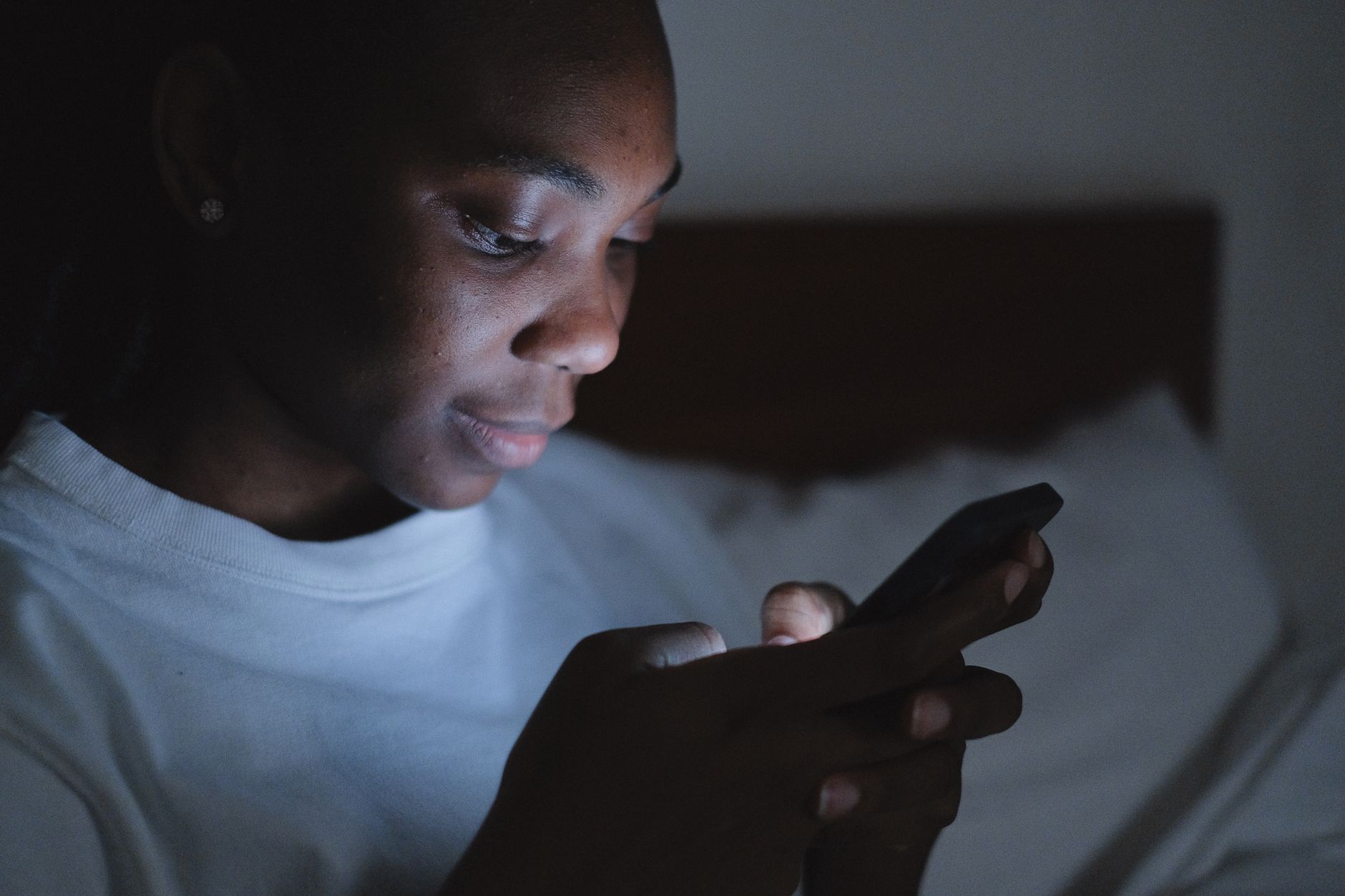 A person's face lit by the blue light of a smartphone in a dark room at night.