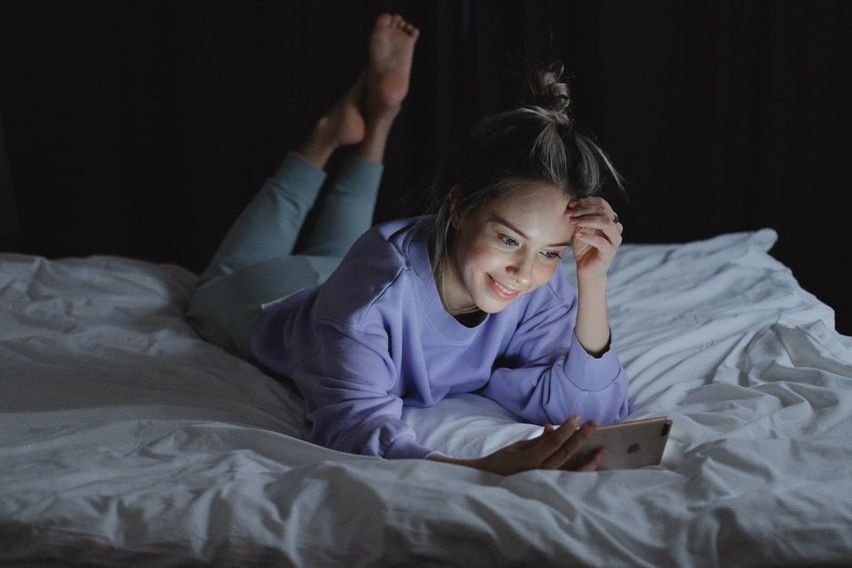 Does Mouth Taping Actually Help with Snoring and Sleep Apnea? Woman happily using smartphone in bed at night. Cozy and relaxed setting.