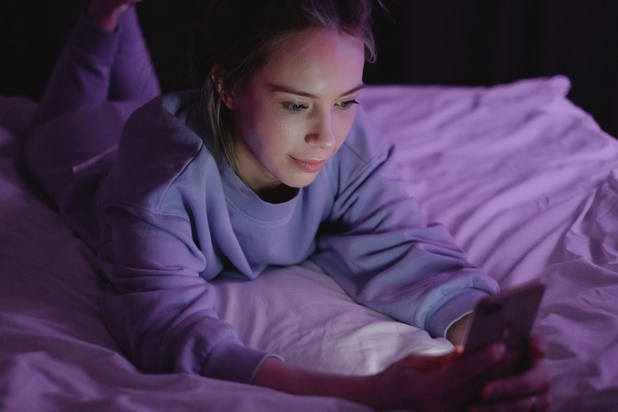 person using phone in bed at night disrupting sleep recovery and melatonin production