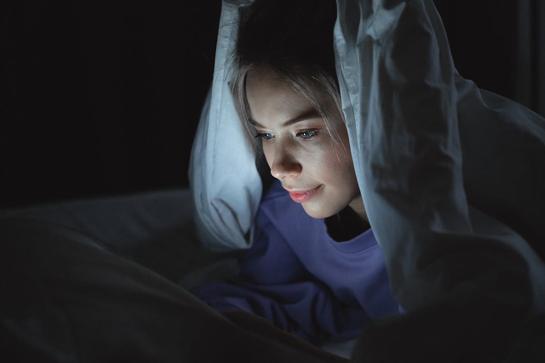 Free Woman Lying on Bed  Using a Gadget Stock Photo