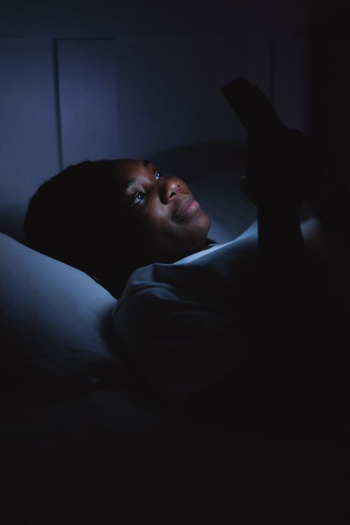 Free A woman lying in bed at night, using her smartphone with dim lighting. Stock Photo
