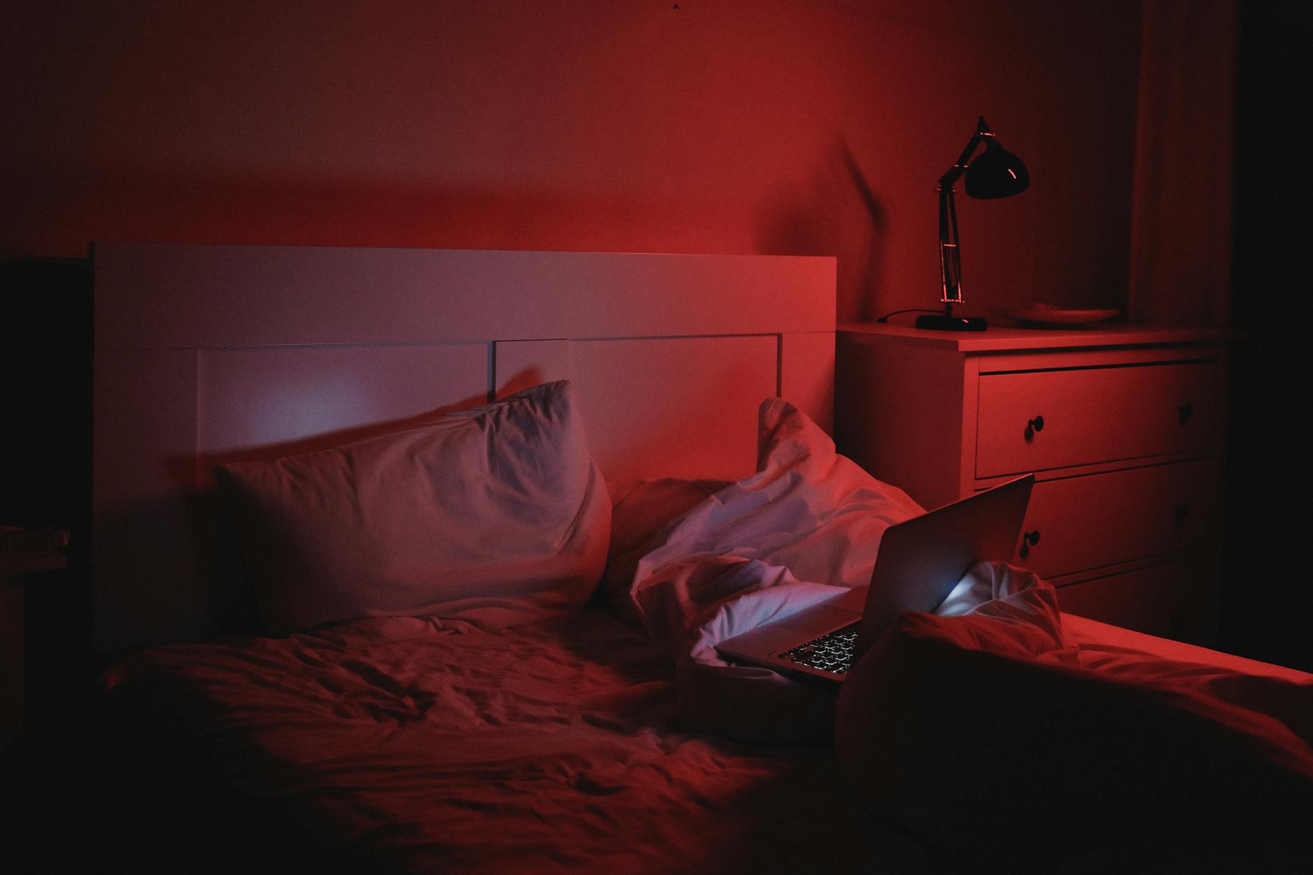 A dimly lit bedroom scene featuring a cozy bed with a laptop and a warm ambiance.