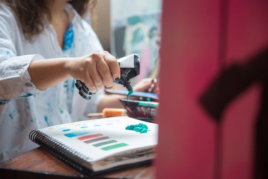 Artist squeezing vibrant green paint onto a sketchbook indoors in natural light.