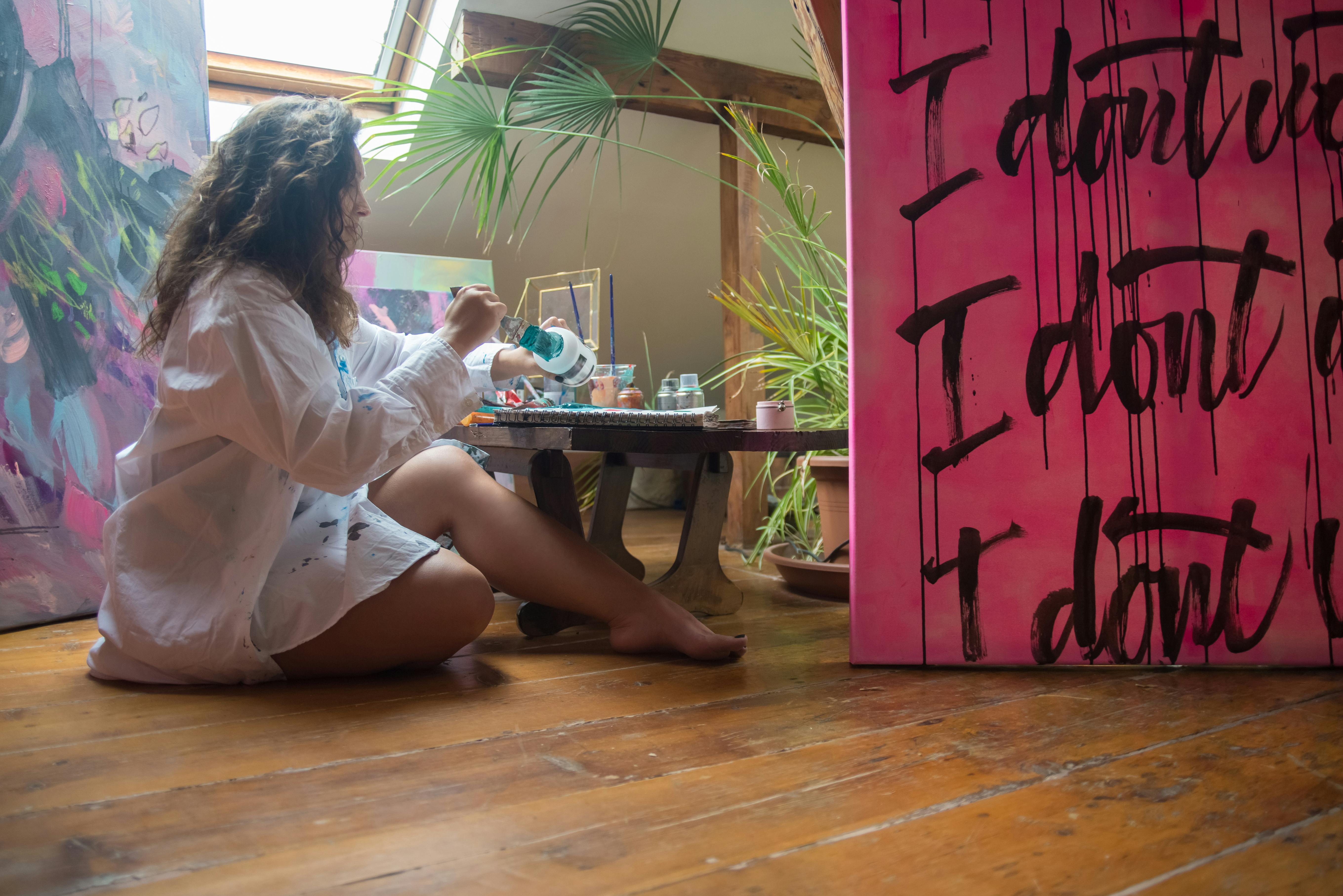 Female artist in sunlit studio painting on canvas with vibrant colors. Captivating indoor scene.