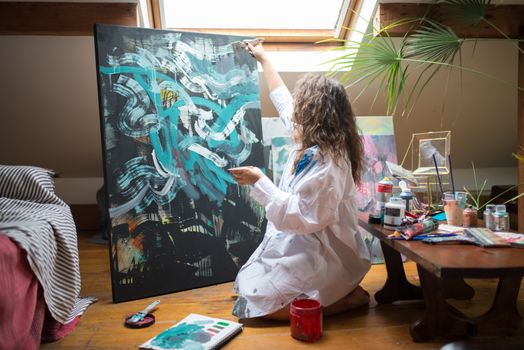 An artist creates abstract art on a large canvas in a cozy attic studio.