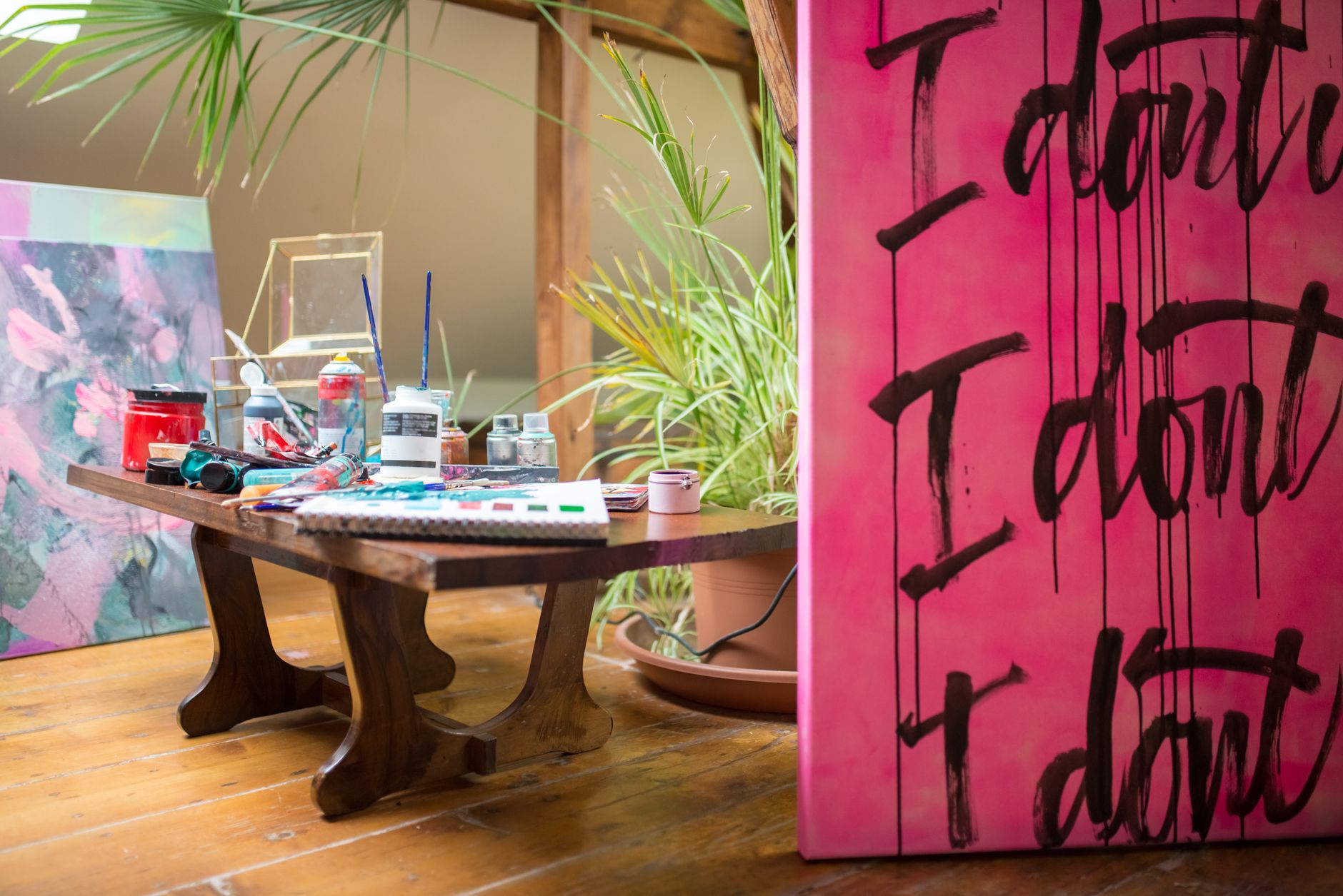 Art studio in Portugal with vibrant paintings and numerous art supplies on a wooden table.