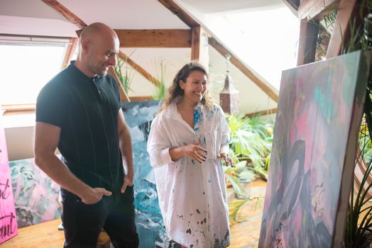 An artist and a viewer enjoy a vibrant painting in a sunny loft studio.