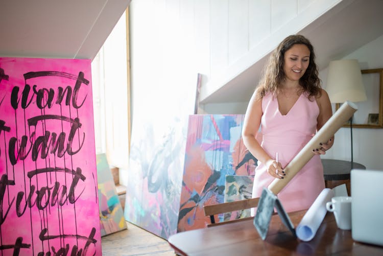 Smiling Artist With Poster In Tube In Home Workshop