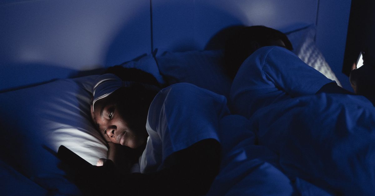 Person sleeping with phone on pillow next to them, blue light glowing