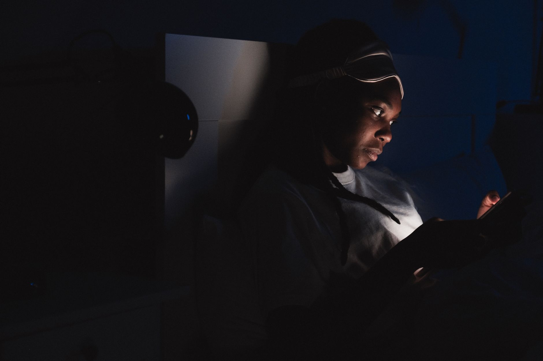 Giovane sdraiato al buio, viso illuminato dallo schermo di un tablet tenuto con entrambe le mani