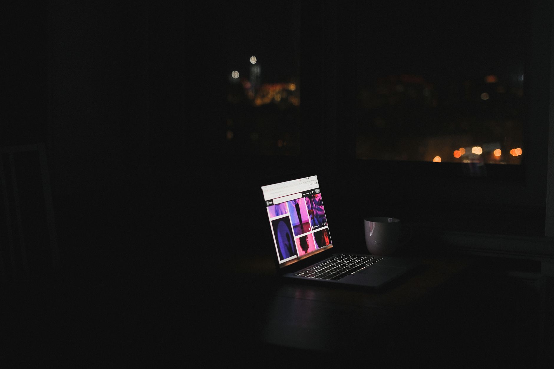 Ordenador portátil encendido en una habitación oscura, de noche, con una taza junto al teclado