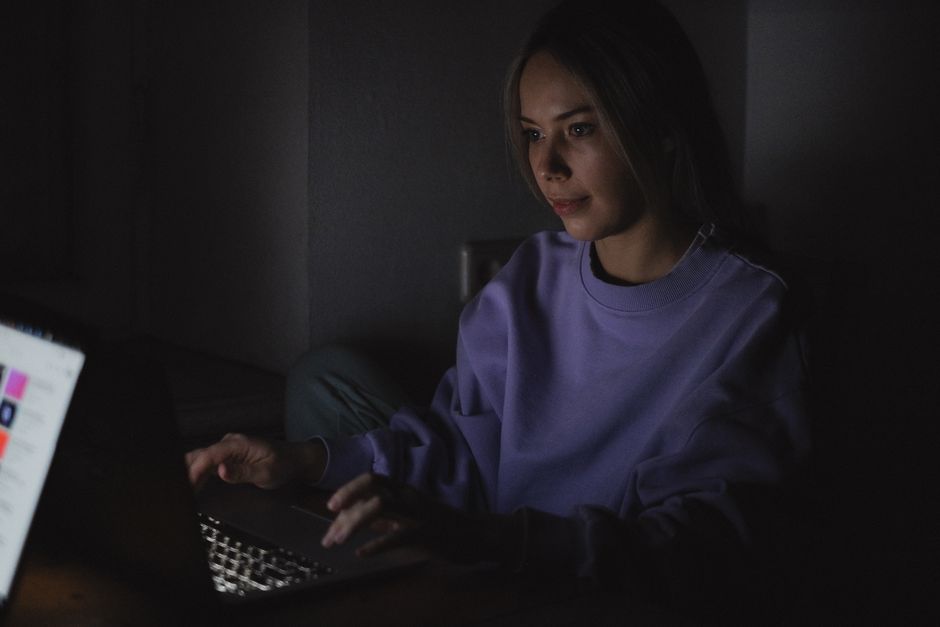 Calm vs Headspace: Sleep Meditation Effectiveness Uncovered (2024) A woman wears a sweater and uses a laptop in a dark room, creating a focused and calm atmosphere.