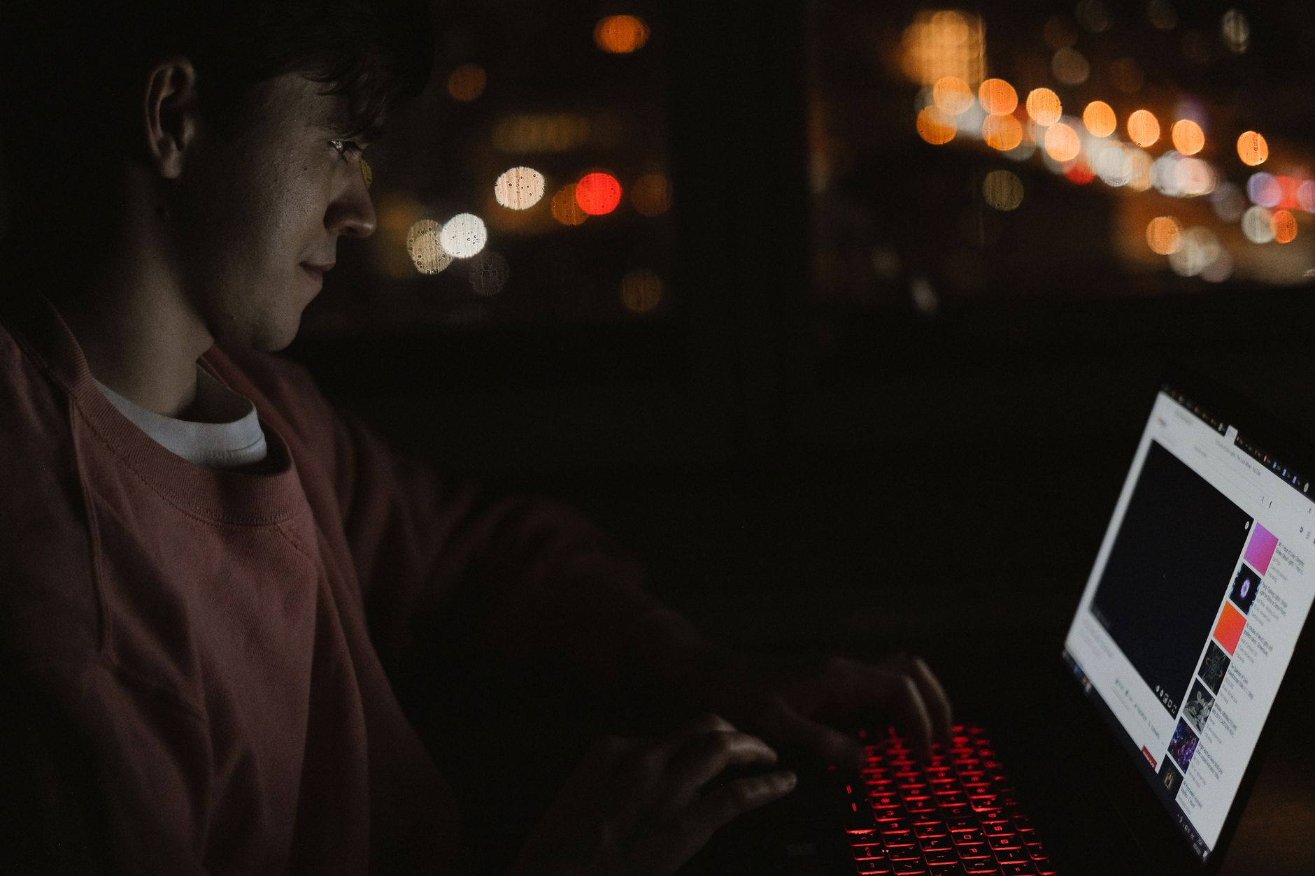 Jeune homme devant un ordinateur portable rétroéclairé la nuit, lumières de la ville floues en arrière-plan