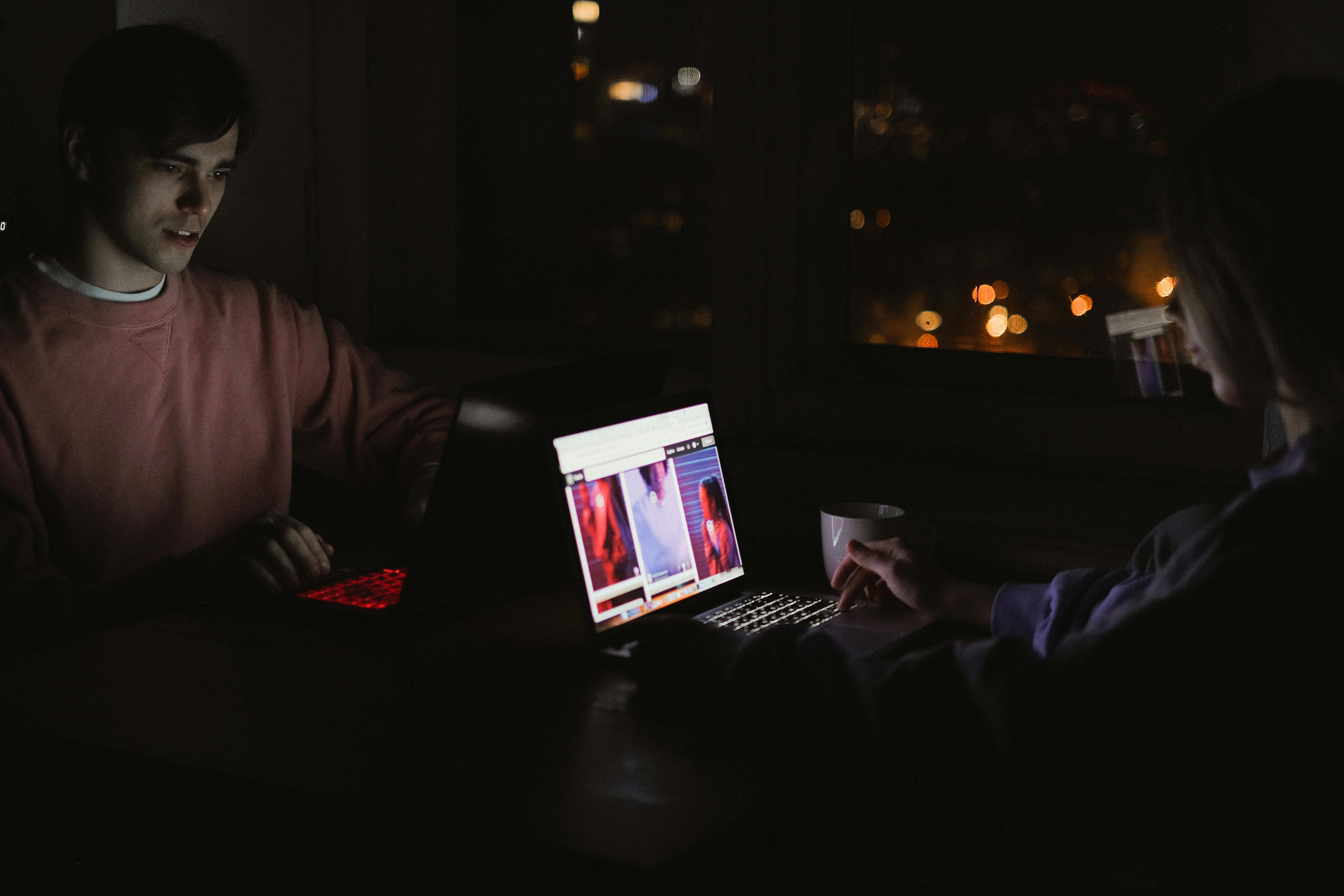 young people sitting in front of laptops in the dark