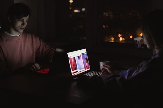 A man and woman using laptops at night, illuminated by screens in a dark, cozy room.