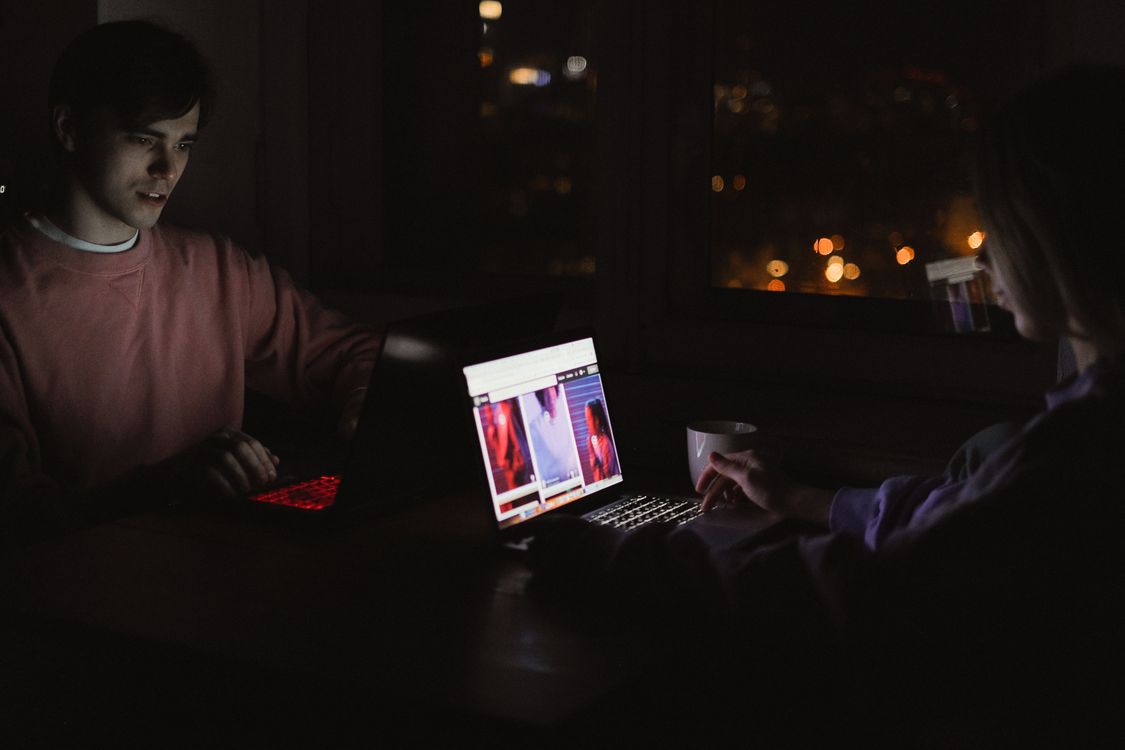 Two people working on laptops at night, screens illuminating a website development workspace