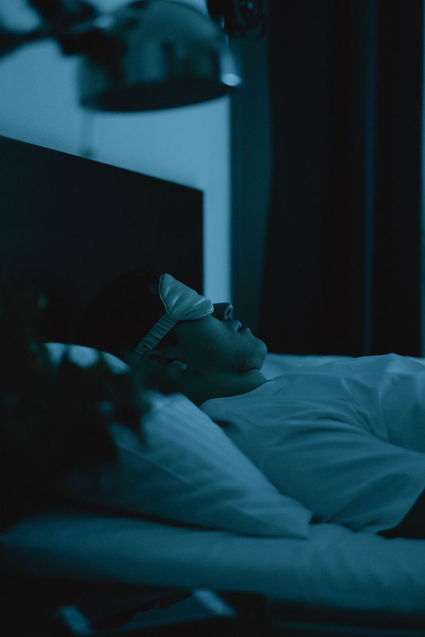 Adult resting in bed wearing a sleep mask in dim light.