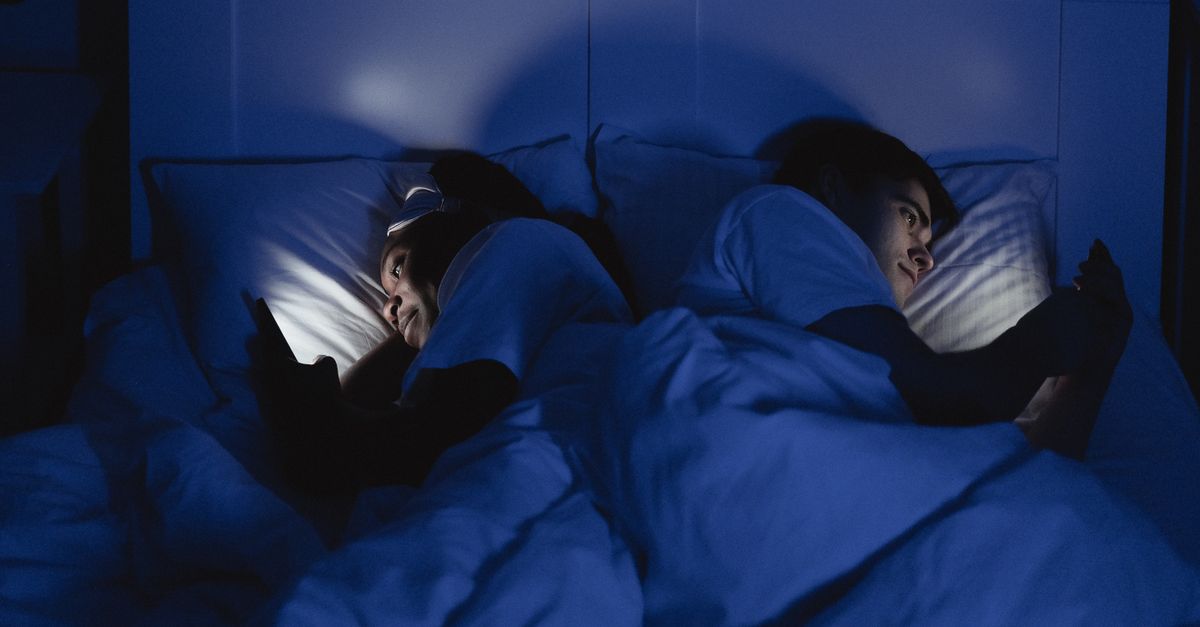 Stel in bed, beiden verlicht door hun telefoonscherm