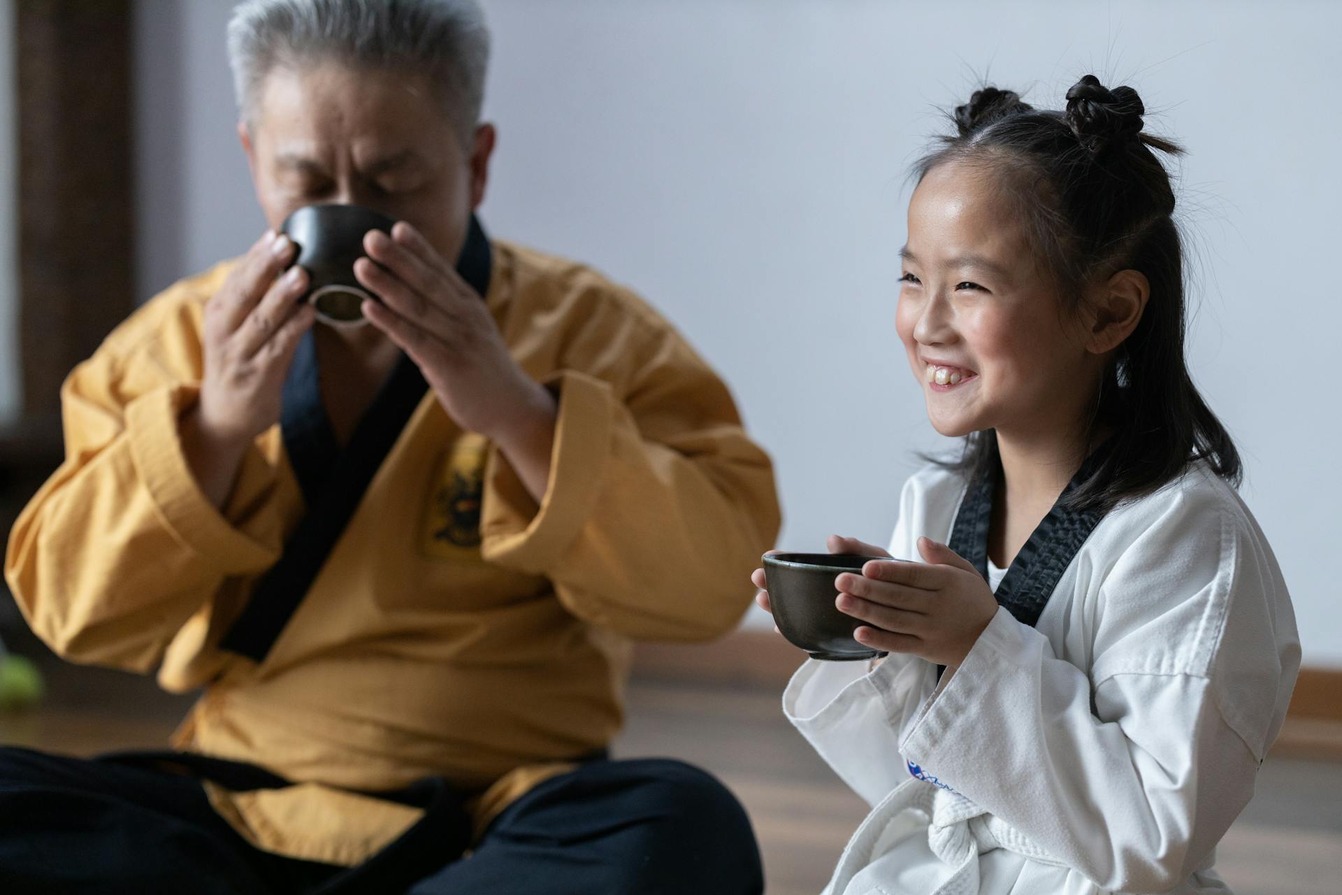 Elderly Man Drinking On Bowl Beside A Smiling Girl