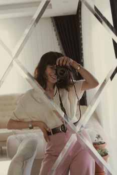 Stylish woman taking a selfie in a mirror with a DSLR camera indoors.