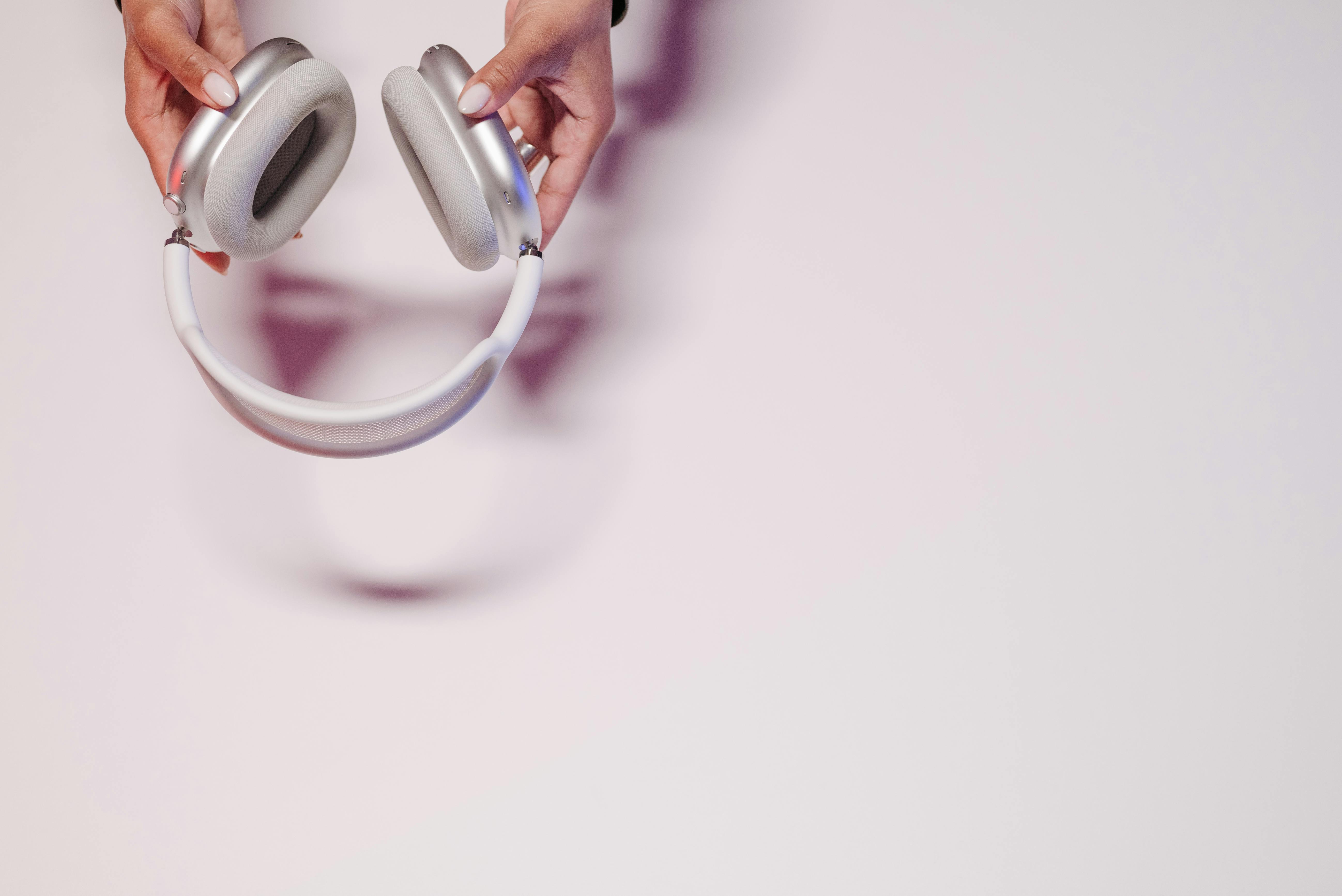 Close-up view of hands holding silver headphones on a soft background, emphasizing modern technology.