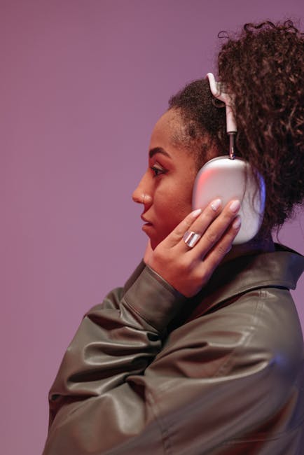 Profile of a young woman wearing headphones, enjoying music against a pink background.