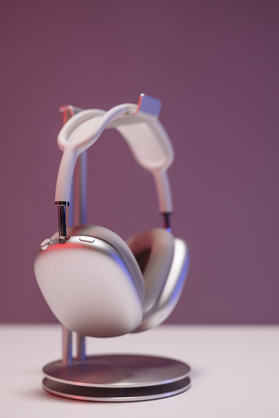 Silver over-ear headphones on a stand against a soft mauve backdrop
