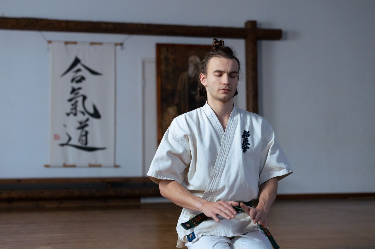 man in martial arts uniform meditating in a dojo with peaceful express