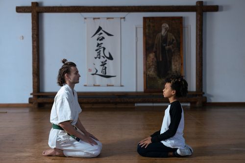 Free A karate trainer and child meditating on a wooden floor in a dojo setting. Stock Photo
