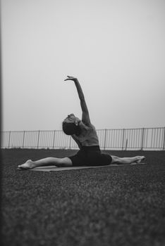 A woman performs a yoga stretch outdoors in black and white, highlighting flexibility and focus.