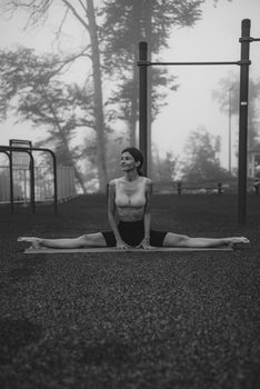 A woman performs a yoga split outdoors in a foggy park, embracing fitness.