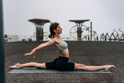 A woman performing yoga splits on a mat outdoors, promoting fitness and flexibility.