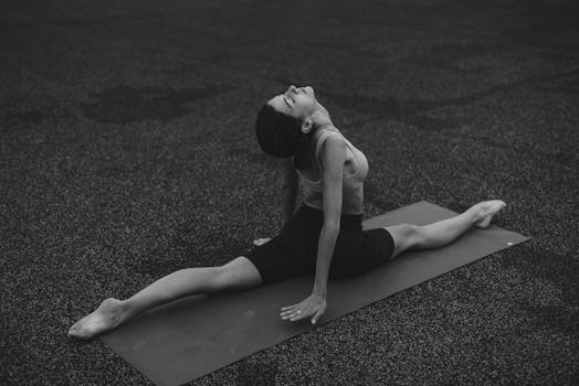 Woman performing yoga split on mat in a serene outdoor environment.