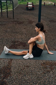 A woman in activewear performs a seated yoga stretch on an outdoor mat.