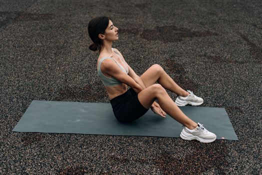 Woman sitting on yoga mat outdoors in an urban setting, embodying fitness and relaxation.