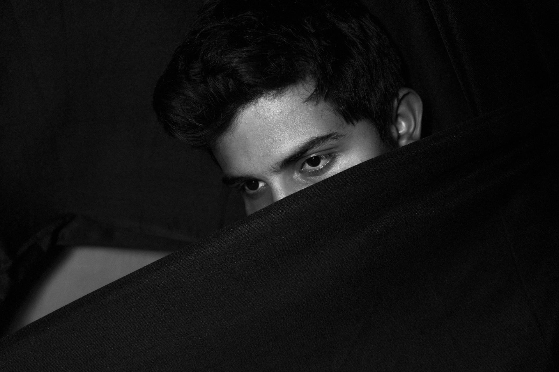 Moody portrait of a man partially obscured by fabric in low light setting.